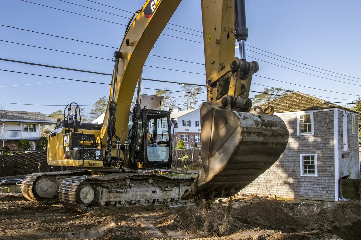 Excavator bucket placing soil during a foundation dig at a house site