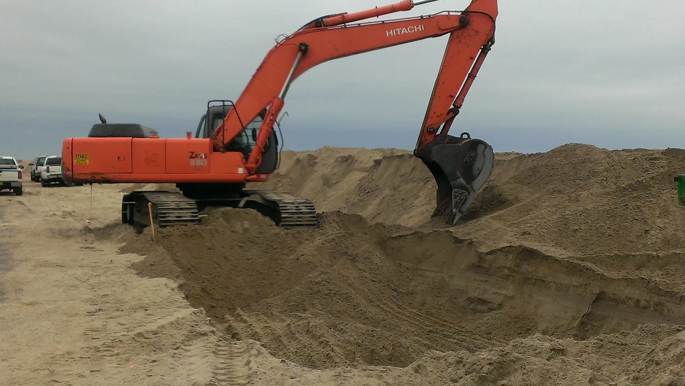 Excavator digging a deep trench in sandy soil